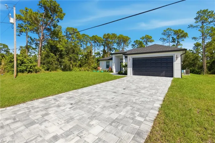 View of front of home with a front yard, decorative driveway, and an attached garage
