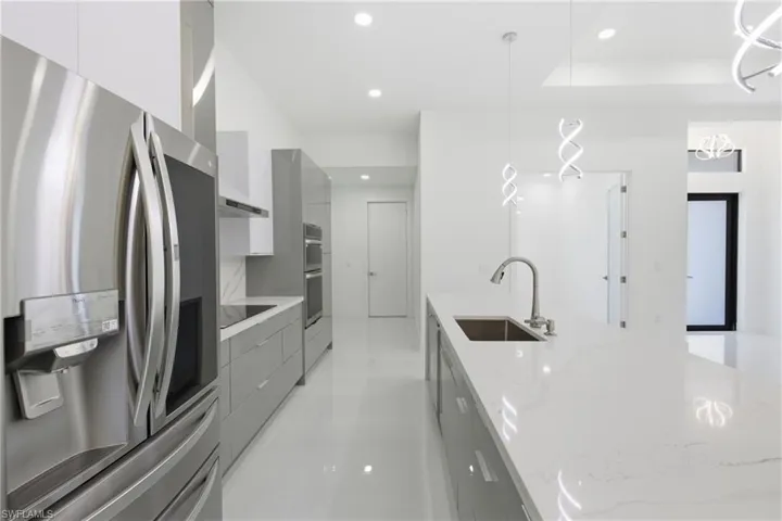 Two tone kitchen featuring modern cabinets, stainless steel appliances, decorative light fixtures, light stone counters, and two tone cabinetry