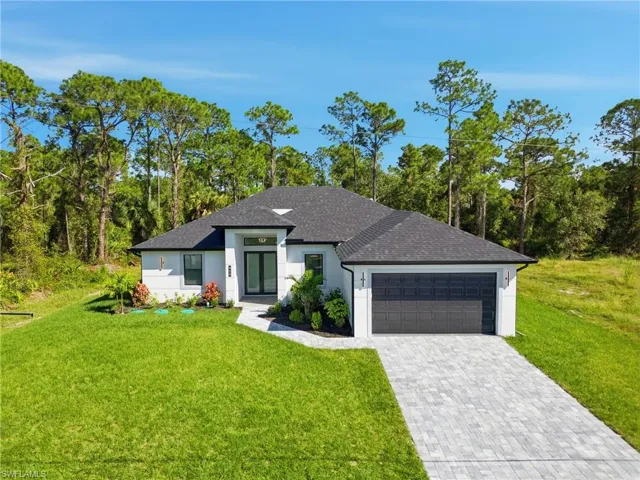 View of front of property with roof with shingles, a front lawn, decorative driveway, a garage, and view of scattered trees