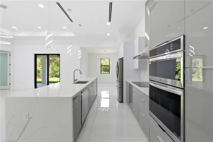 Kitchen featuring modern cabinets, stainless steel appliances, light stone countertops, and hanging light fixtures