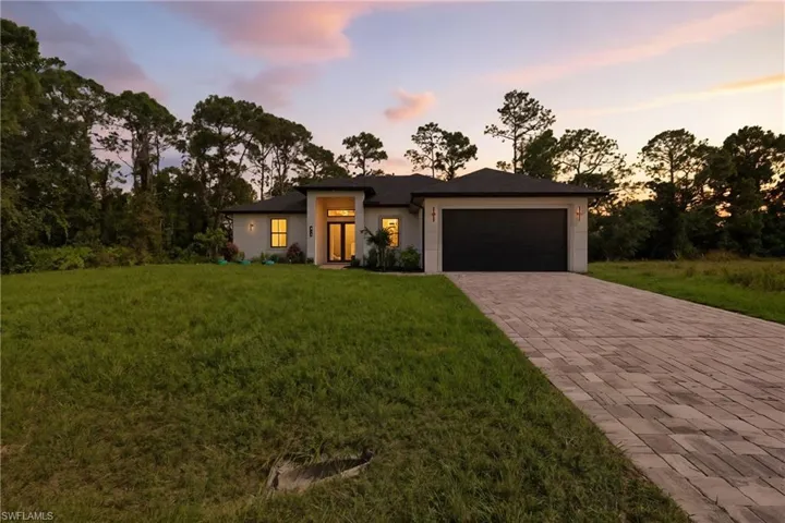 Prairie-style house featuring a lawn, decorative driveway, stucco siding, a garage, and view of wooded area