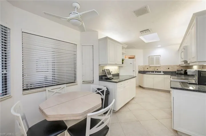 Kitchen featuring white cabinets, open shelves, dark stone counters, a ceiling fan, and white appliances