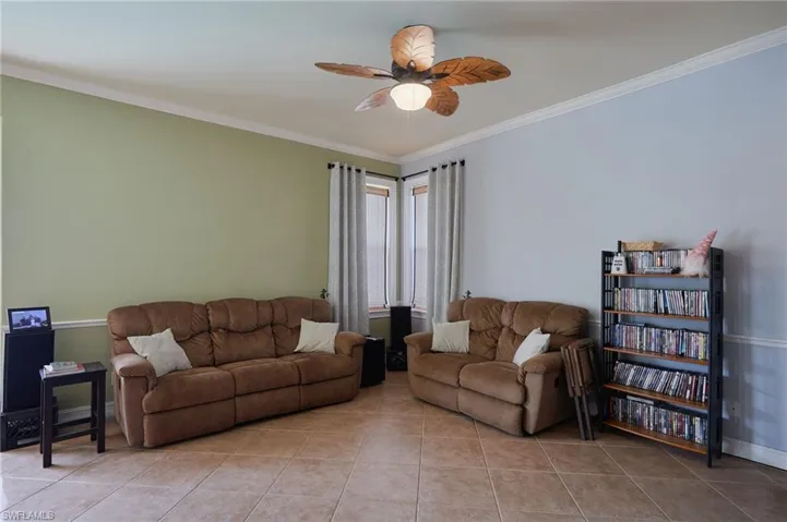 Living room with light tile patterned floors, ceiling fan, and ornamental molding