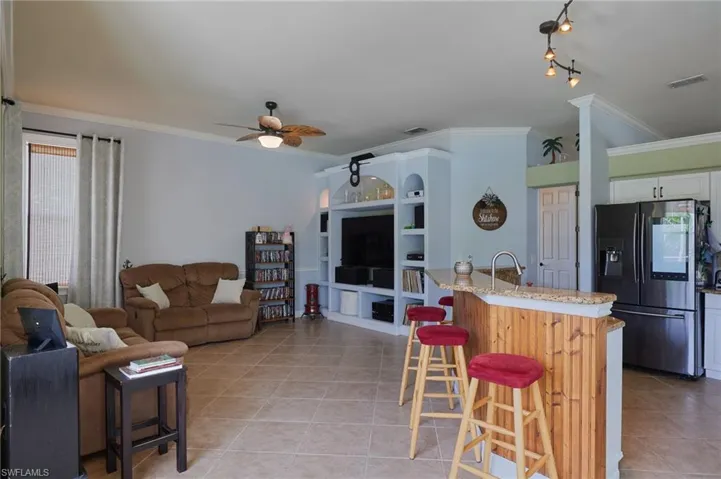 Living room featuring light tile patterned flooring, a ceiling fan, ornamental molding, and built in shelves