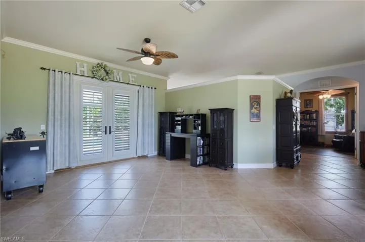 Tiled living room featuring a ceiling fan, crown molding, arched walkways, and french doors