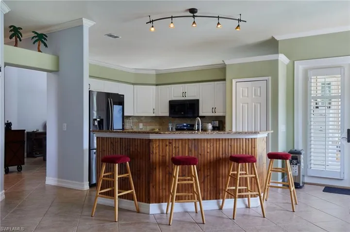 Kitchen with tasteful backsplash, black microwave, white cabinetry, ornamental molding, and a breakfast bar area