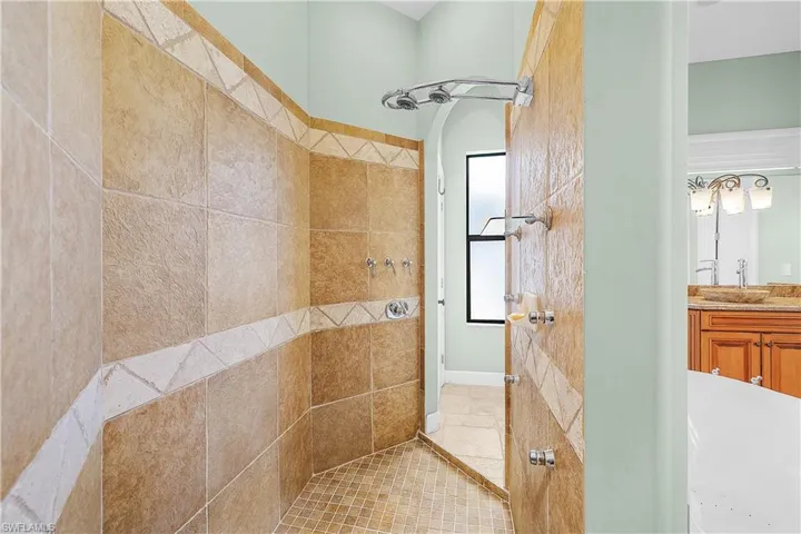 Expansive walk-in shower featuring large format wall tiling with decorative accent bands, mosaic floor tiling, and multiple shower fixtures