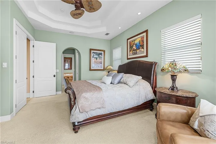 Spacious room featuring tray ceiling, recessed lighting, arched doorway, and light carpeting