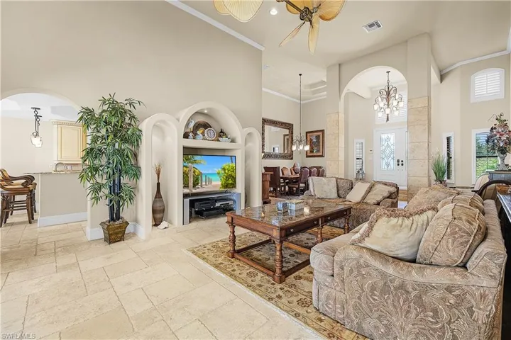 Spacious living area featuring high ceilings, light-toned tile flooring, and decorative arched built-in shelving