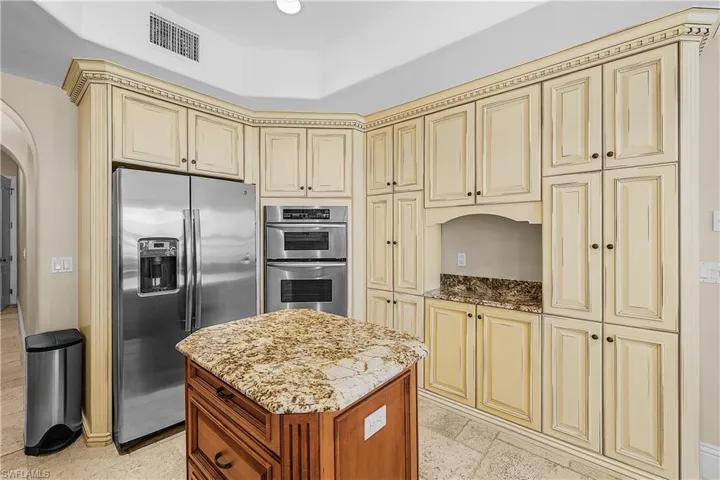 Gourmet kitchen featuring extensive cream-colored cabinetry with decorative crown molding, a central island with a granite countertop, stainless steel appliances including a built-in double oven, and tiled flooring