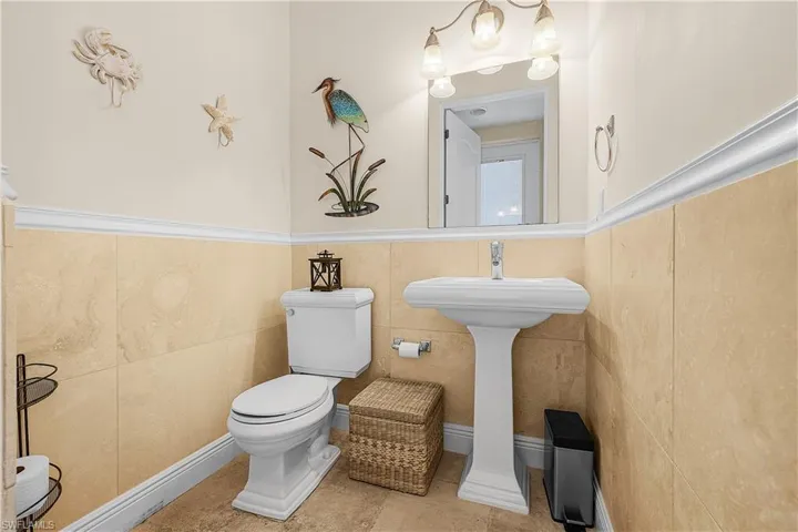 1/2 Bath with pedestal sink with a polished chrome faucet, set against a backdrop of neutral-toned wall tiling and crown molding