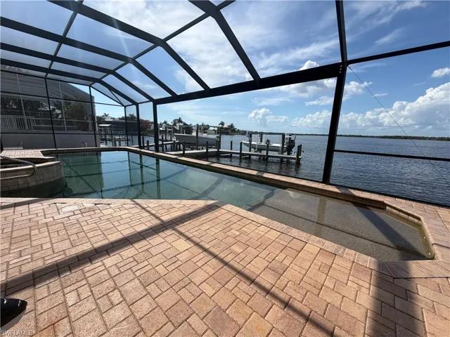 Screened outdoor pool area featuring a rectangular pool, integrated spa, and brick paver patio