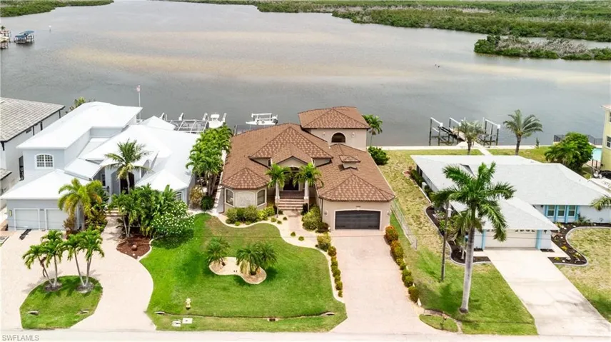 Waterfront residence featuring a private boat dock, lush landscaping, a paved driveway, a two-car garage, and a tiled metal roof