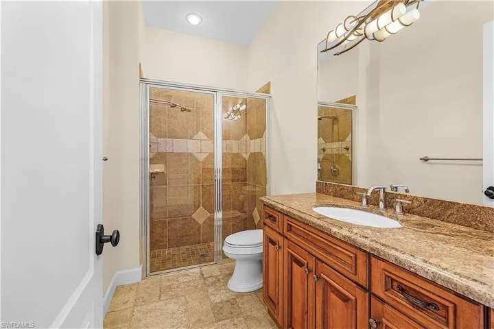 Bathroom featuring a wood vanity with a stone countertop, an undermount sink, and a framed mirror