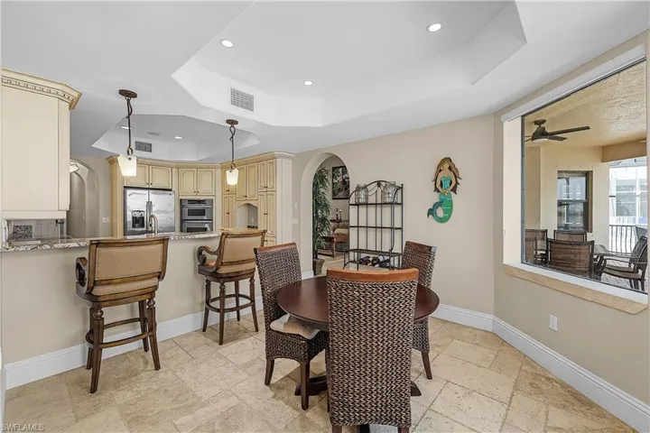 Kitchen and dining area featuring tray ceilings with recessed lighting, tile flooring, an eat-at kitchen island with granite-style countertops, stainless steel appliances, and a window overlooking an outdoor patio