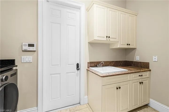Utility room featuring a built-in sink with a stone-finish countertop, matching base cabinetry, and overhead storage cabinets