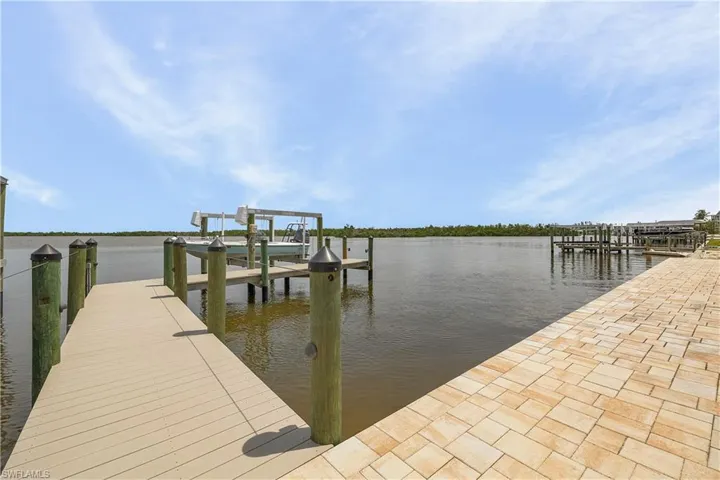 Waterfront property featuring a composite deck dock, a boat lift, and a paver decking behind home