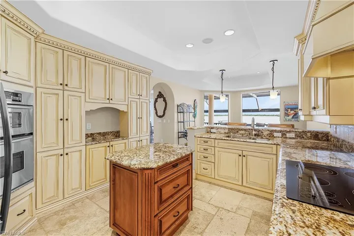 Gourmet kitchen with extensive cream-toned cabinetry, a built-in double oven, and a central wood-finish island with a stone countertop