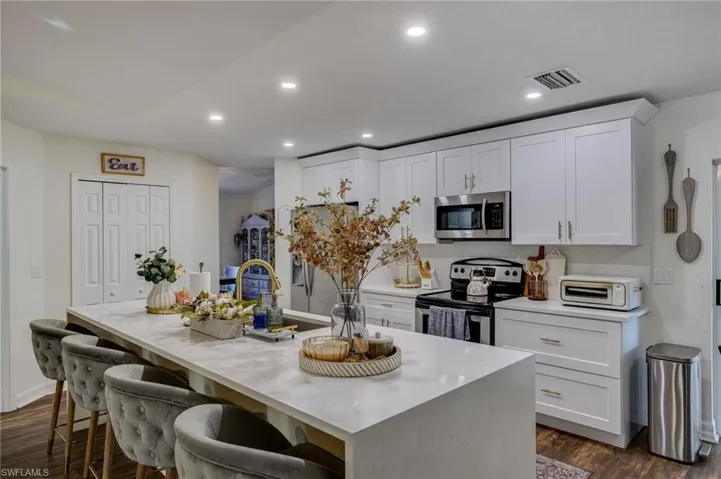 Kitchen with appliances with stainless steel finishes, a kitchen breakfast bar, white cabinets, an island with sink, and dark wood-type flooring