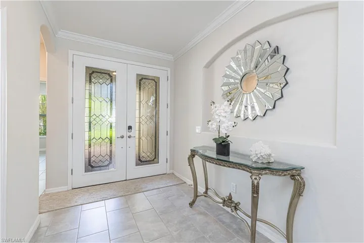 Foyer with french doors, arched walkways, crown molding, and light tile patterned floors