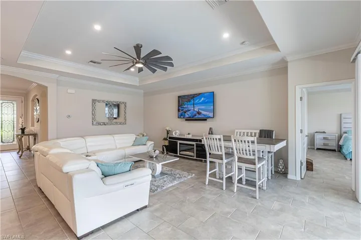 Living area featuring crown molding, arched walkways, ceiling fan, and a raised ceiling