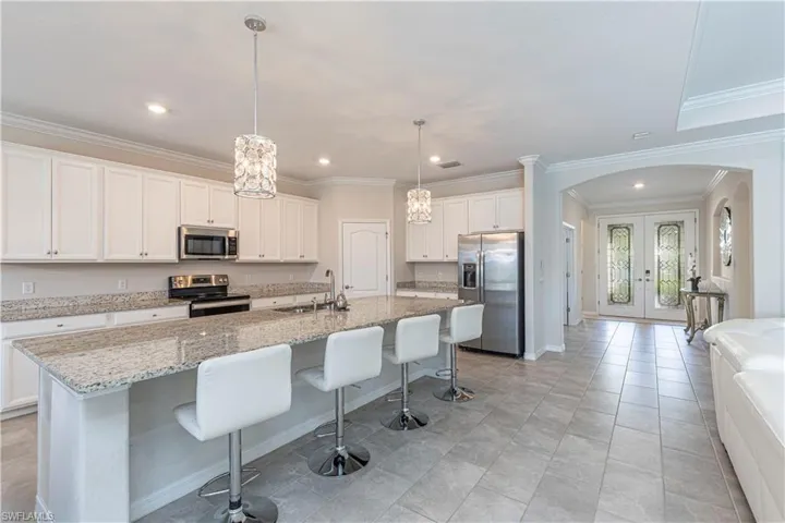 Kitchen with arched walkways, french doors, stainless steel appliances, a center island with sink, and white cabinetry