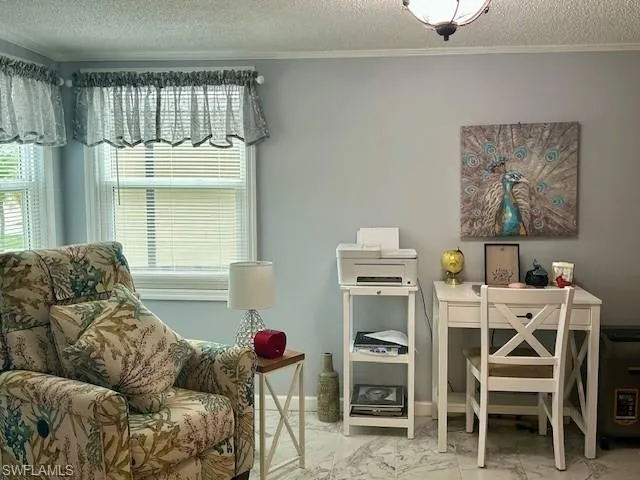 Sitting room featuring marble look tile flooring, crown molding, and a textured ceiling