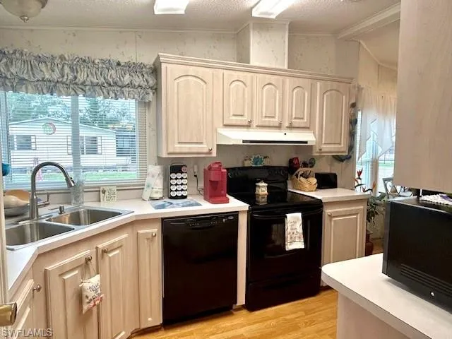 Kitchen featuring black appliances, extractor fan, light wood finished floors, crown molding, and light countertops