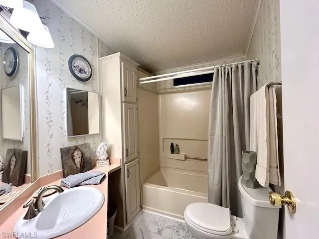 Full bathroom featuring wallpapered walls, a textured ceiling, shower / bath combo with shower curtain, and marble finish floors