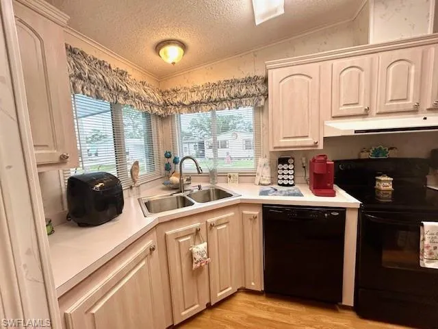 Kitchen with black appliances, under cabinet range hood, a textured ceiling, light wood-style flooring, and light countertops