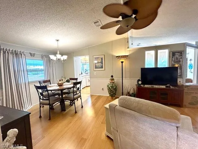 Dining room with bamboo wood finished floors, a chandelier, a textured ceiling, vaulted ceiling, and a ceiling fan