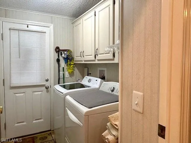 Washroom with cabinet space, washing machine and dryer, crown molding, and a textured ceiling