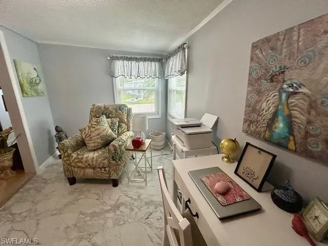 Sitting room with crown molding, light marble finish floors, and a textured ceiling