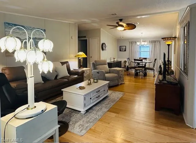 Living room featuring ceiling fan, a chandelier, light wood-type flooring, and ornamental molding