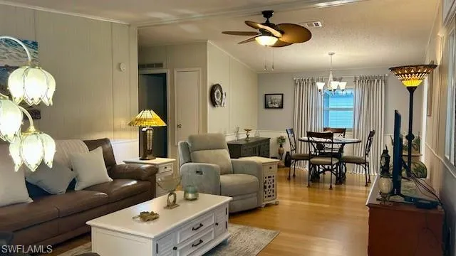 Living room with a chandelier, light wood-type flooring, ornamental molding, and a ceiling fan