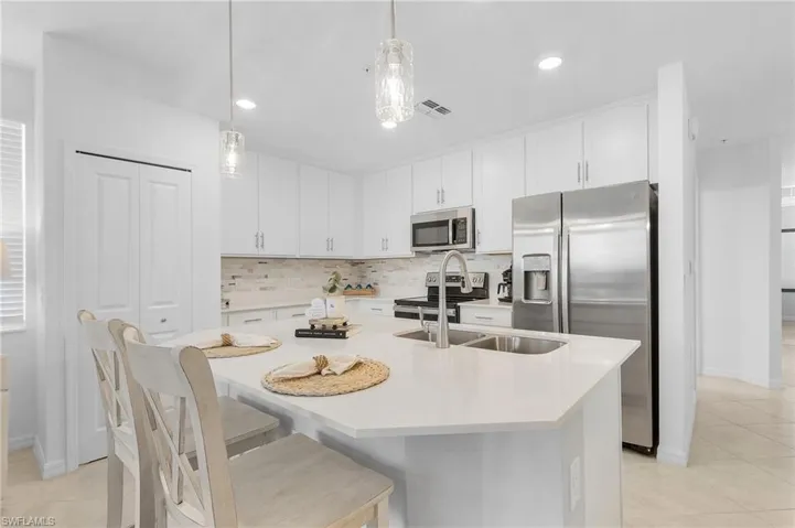 Kitchen with a kitchen island with sink, white cabinetry, pendant lighting, and appliances with stainless steel finishes