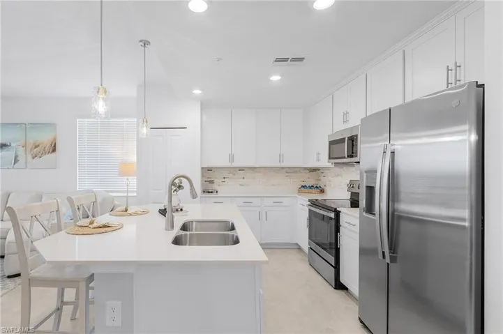 Kitchen with white cabinetry, sink, appliances with stainless steel finishes, and an island with sink