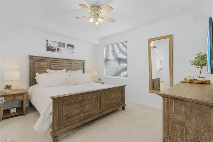 Bedroom with ceiling fan, light colored carpet, and ensuite bath