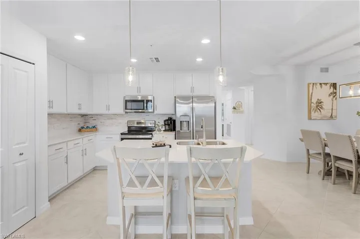 Kitchen with decorative backsplash, stainless steel appliances, decorative light fixtures, a center island with sink, and white cabinetry