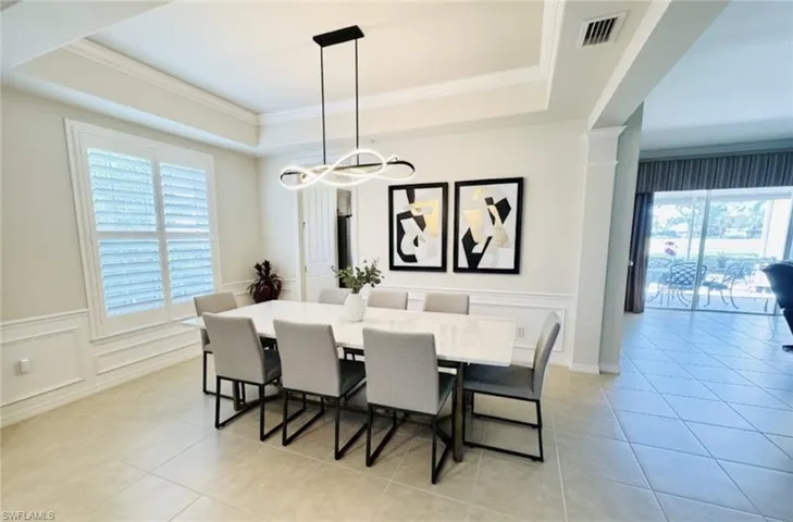 Dining area with a decorative wall, a wainscoted wall, ornamental molding, light tile patterned floors, and a raised ceiling. *Photos have been virtually staged for perspective.