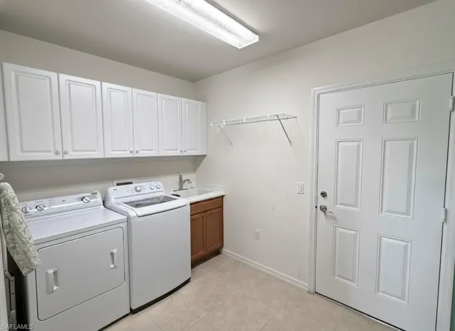 Laundry area with washer and clothes dryer, light tile patterned floors, and cabinet space