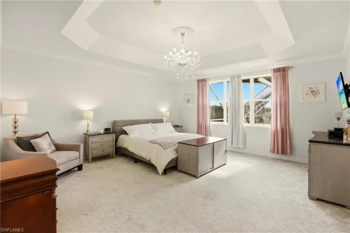 Bedroom featuring light carpet, a tray ceiling, ornamental molding, and a chandelier