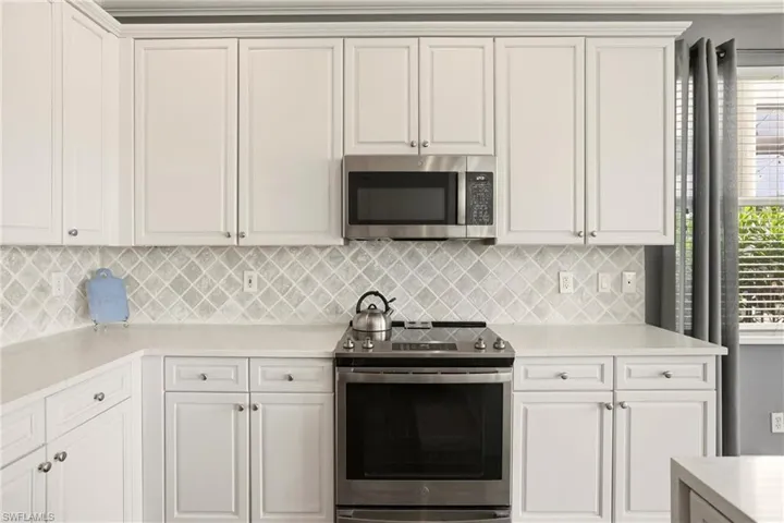 Kitchen featuring appliances with stainless steel finishes, white cabinetry, light stone countertops, and backsplash