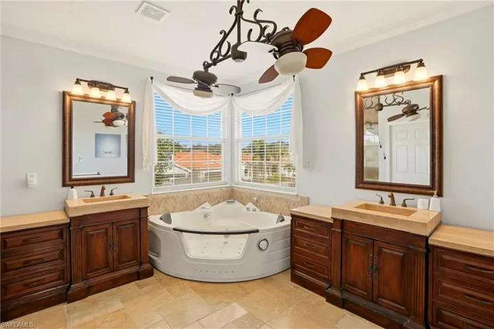 Full bath featuring two vanities, a tub with jets, ornamental molding, and stone tile flooring
