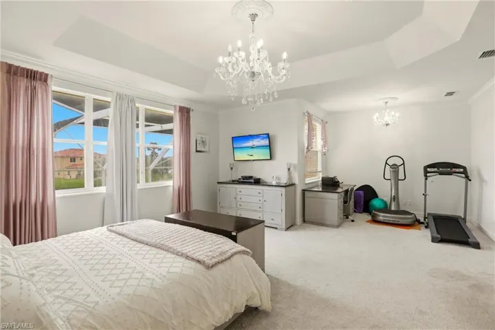 Carpeted bedroom with a chandelier, a tray ceiling, and ornamental molding