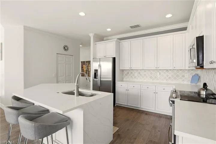 Kitchen featuring appliances with stainless steel finishes, white cabinetry, light stone counters, crown molding, and a center island with sink