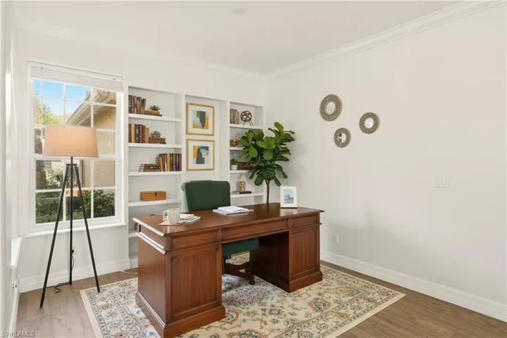 VIRTUAL STAGED Office area with crown molding, light wood-style floors, and built in shelves