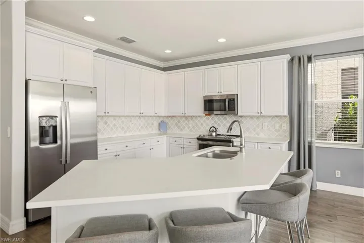 Kitchen featuring appliances with stainless steel finishes, white cabinets, a kitchen bar, a center island with sink, and recessed lighting