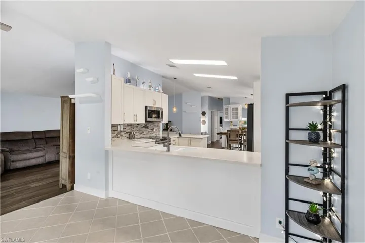 Kitchen featuring vaulted ceiling, backsplash, stainless steel microwave, light tile patterned flooring, and white cabinetry