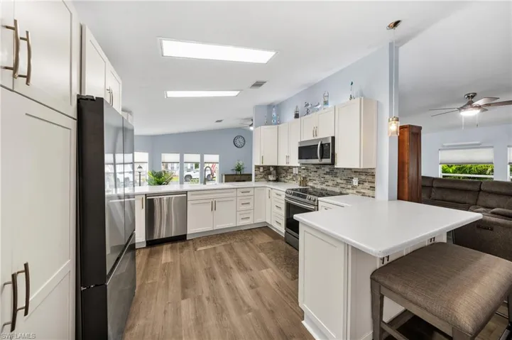 Kitchen with a ceiling fan, a peninsula, open floor plan, white cabinets, and vaulted ceiling